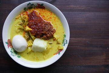 Lontong, a traditional Southeast Asian dish of compressed rice cakes in rich coconut curry, served with lodeh, sambal kacang, sambal tumis, hard-boiled eggs, and fresh vegetables on a decorative plate