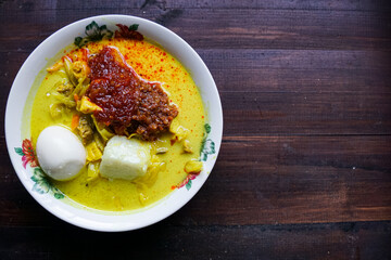 Lontong, a traditional Southeast Asian dish of compressed rice cakes in rich coconut curry, served with lodeh, sambal kacang, sambal tumis, hard-boiled eggs, and fresh vegetables on a decorative plate
