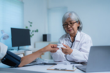 Senior female doctor is measuring blood pressure of a patient while holding a pulse oximeter in her...