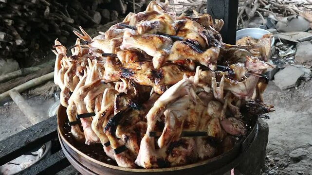 A pile of cooked grilled chicken is drained on a bamboo tray in a simple and traditional kitchen. It looks very delicious and tempting.
