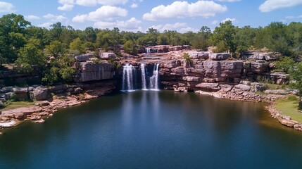 Fototapeta premium Aerial view Waterfall cascading into a lake, surrounded by lush greenery under a partly cloudy sky