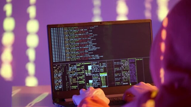 A hacker in a hooded sweatshirt writes code on a laptop terminal with system logs, network data, and commands under purple neon light. Cybersecurity threat, hacking, and data breach implied