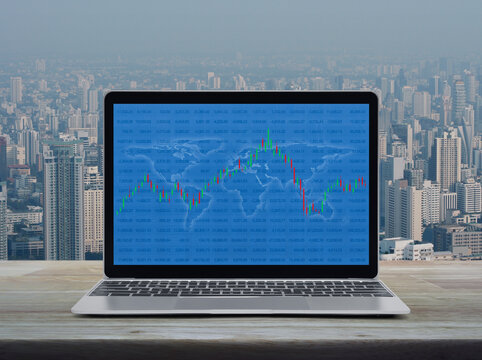 Trading graph of stock market with world map and graph on laptop computer on wooden table over city tower and skyscraper, Business investment online concept, Elements of this image furnished by NASA