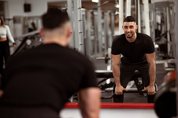 Junger Mann, trainiert mit einer langen Hantel vor dem Spiegel im Fitness Center. Krafttraining. Lächeln.