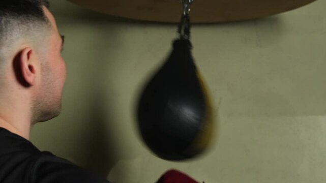 Boxer practices hitting speed bag focusing on technique. Guy performs training and practices professional skills flexing arm muscles in special gym