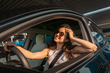 Happy and excited woman sitting in the car on a day trip in the summer, wearing sunglasses. Travel...