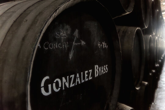 Close-up, low-light view of wooden sherry wine barrels for preservation at a traditional winery with the Gonzalez Byass Tio Pepe brand painted on the barrel.