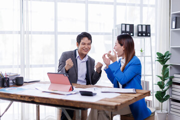 Successful business people giving each other a high five in a meeting. Two young asian business professionals celebrating teamwork in an office.
