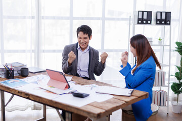 Successful business people giving each other a high five in a meeting. Two young asian business professionals celebrating teamwork in an office.
