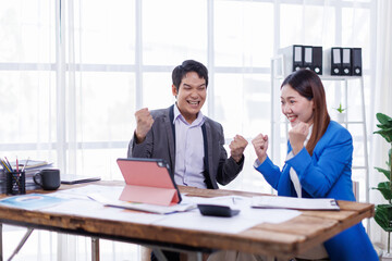 Successful business people giving each other a high five in a meeting. Two young asian business professionals celebrating teamwork in an office.
