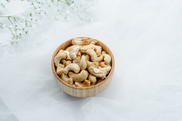 Cashew nuts in a wooden bowl on a white background with floral accents