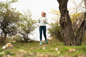 Young happy woman trail runner cross country running in mountains, jogging along trails outdoors,...