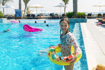 Portrait of smiling little girl in swimming pool on summer vacation.