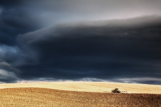 Dark clouds over tractor in a crop field, Tuscany, Italy