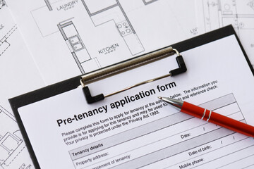 Pen on pre-tenancy application form and planning blueprints of residential building project close up