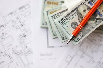 Big amount of US dollars money bills with pen and planning blueprints of residential building...