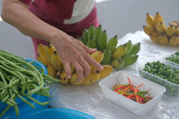 Fresh bananas are carefully arranged at roadside market stall where vibrant green beans and...