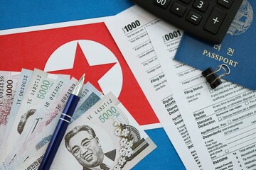 North Korean won money bills lies on table with pen, calculator, passport and tax forms
