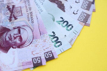 Mexican pesos money bills in big amount lies on yellow color table close up