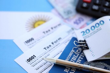 Argentine pesos money bills in big amount lies on table with pen, calculator, passport and tax forms