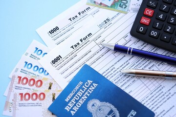 Argentine pesos money bills in big amount lies on table with pen, calculator, passport and tax forms
