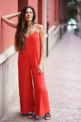 A Fashionable Woman Dressed in a Vibrant Red Jumpsuit Strolling Along an Urban Street