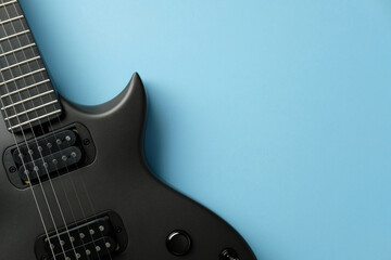 Modern black electric guitar close-up on a light blue background. Ideal for music, instrument, rock, or metal concepts