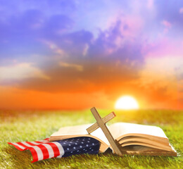Holy Bible, Christian cross and US flag on grass. Sunny day. God Bless America.