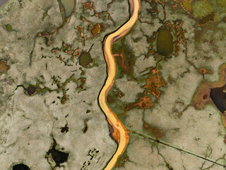 Top-down view of a winding yellow river cutting through a textured marshland with scattered ponds and rich green, orange, and brown patches.