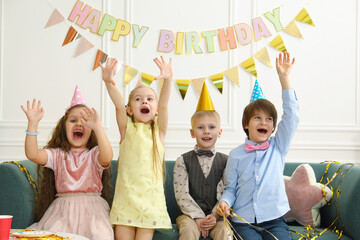 Cheerful children in conical paper hats celebrating birthday indoors. Surprise party