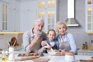 Grandparents and their granddaughter cooking together at white marble table in kitchen