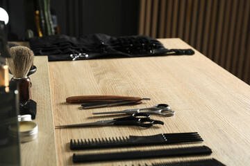 Many different barber's tools on light wooden table in barbershop, closeup