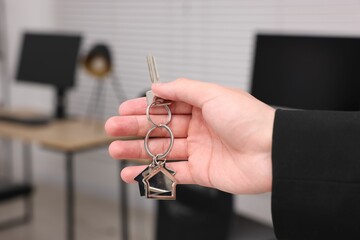 Real estate agent with house key indoors, closeup. Space for text