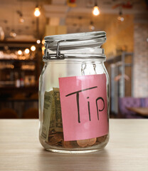 Tips jar with money on light wooden table in cafe
