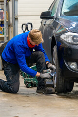 A car service worker changes winter tires to summer wheels on a black automobile. Automotive technician in protective gloves using an impact driver for seasonal tire replacement