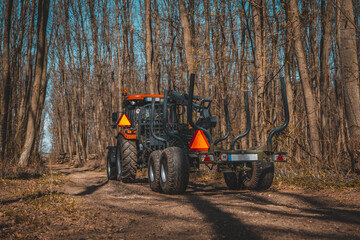 Forwarder tractor for wood transport. Tractor with trailer loaded with logs. Forestry tractor or forestry tractor for harvesting wood in the forest. Spring forest.