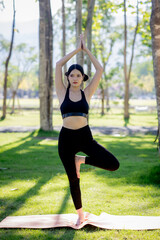 A woman is doing yoga in a garden with trees.