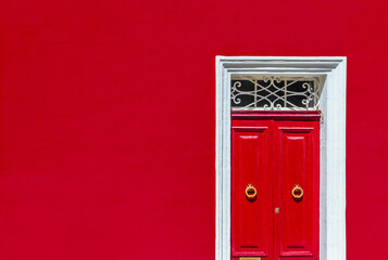 Minimalist architectural photography. Red wall of residential building facade with red door in white wooden frame