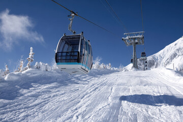 Obraz premium An empty gondola gracefully ascends snowy mountain at ski resort, carrying hopeful skiers and snowboarders towards thrilling adventures