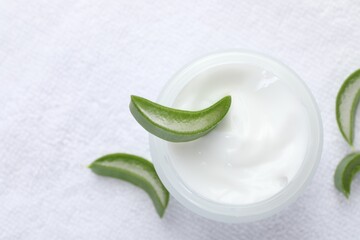 Moisturizing cream with extract of aloe vera and cut leaves on white towel, top view