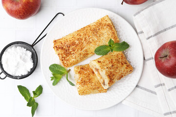 Tasty apple strudels with powdered sugar, mint and fruits on white tiled table, flat lay