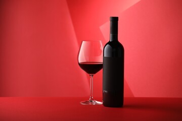 Bottle and glass of tasty wine on red background