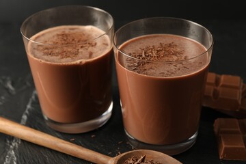 Tasty chocolate milk with shavings and pieces on black table, closeup