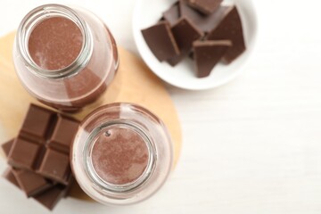Tasty chocolate milk and pieces on white table, flat lay