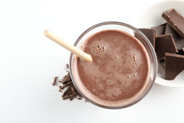 Tasty chocolate milk with shavings and pieces on white table, top view