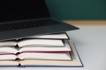 Stack of books and laptop on desk against chalkboard, closeup