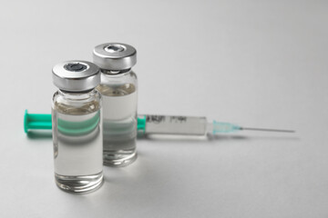 Hepatitis vaccine in glass vials and syringe on grey background, closeup