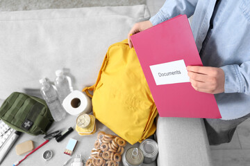 Survival kit. Woman putting documents into backpack indoors, closeup