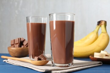 Tasty chocolate milk in glasses, pieces and bananas on blue wooden table, closeup