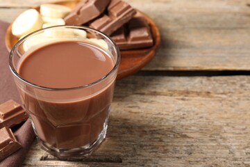 Tasty chocolate milk, pieces and banana on wooden table, closeup. Space for text